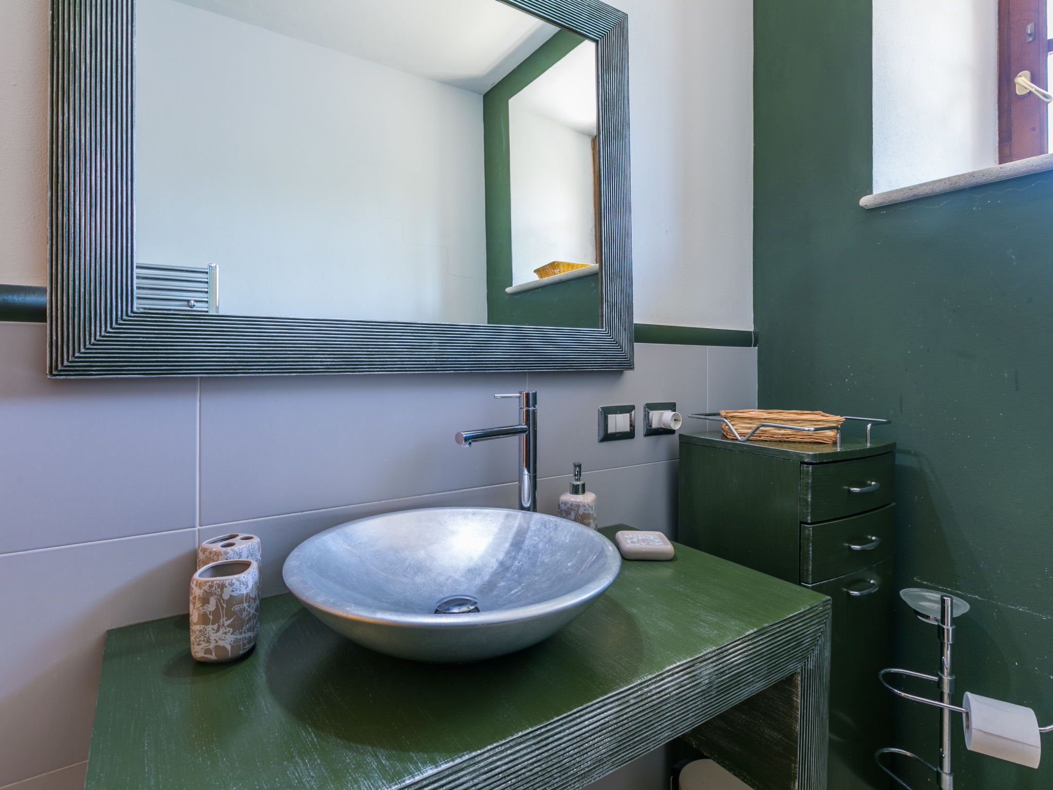 A bathroom with a large mirror, a vessel sink, and a green vanity.
