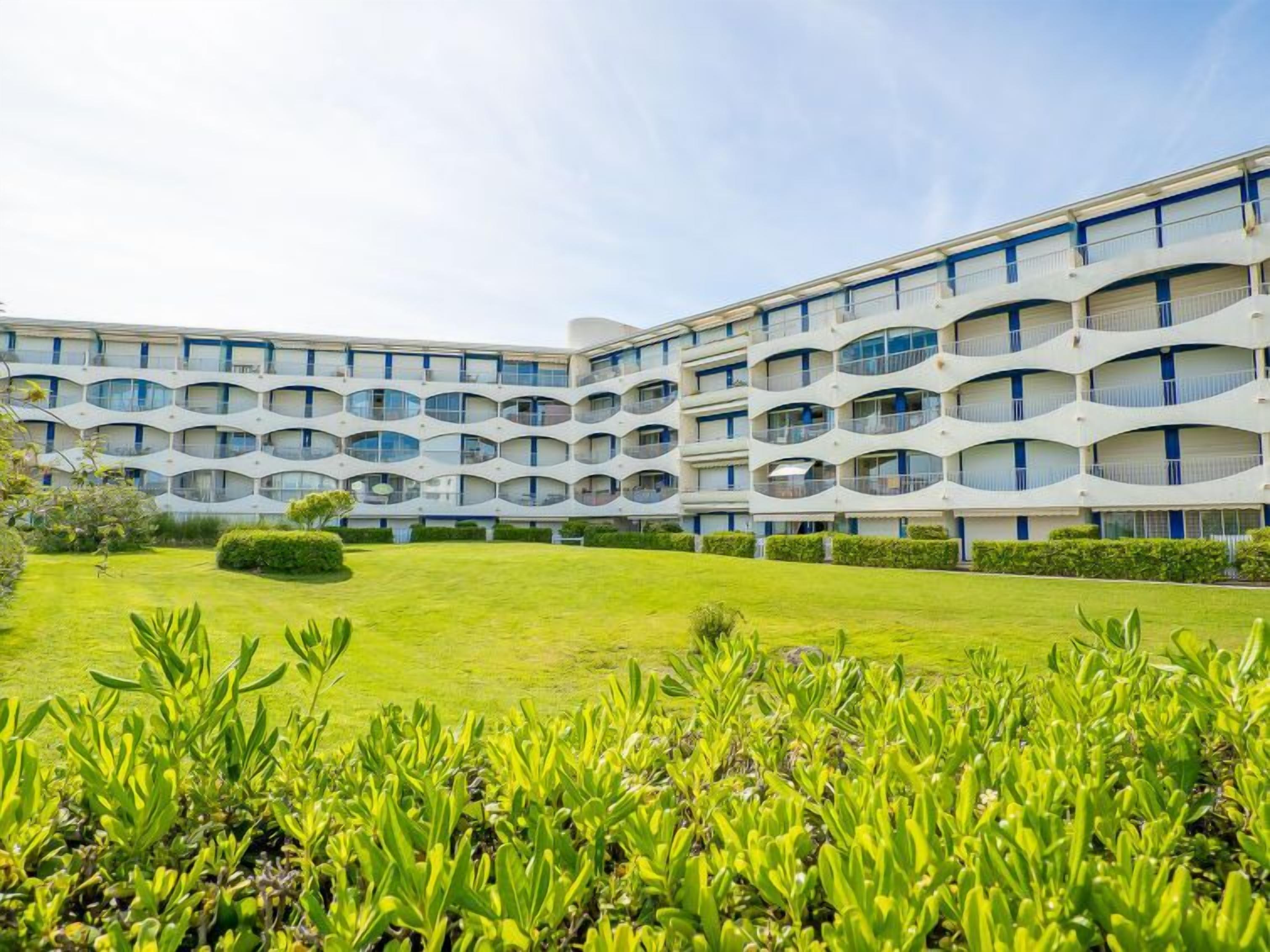 Un edificio moderno con una facciata curva distintiva, numerosi balconi e un prato curato.