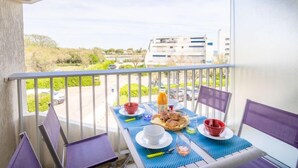 A balcony with a table set for breakfast, including croissants and orange juice, overlooking a parking area and buildings. - Les Terrasses de la Mer by Interhome (La Grande Motte)