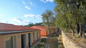 A row of single-story buildings with a red-tiled roof, a stone pathway, and trees in the background. - Borgoverde by Interhome (Imperia)