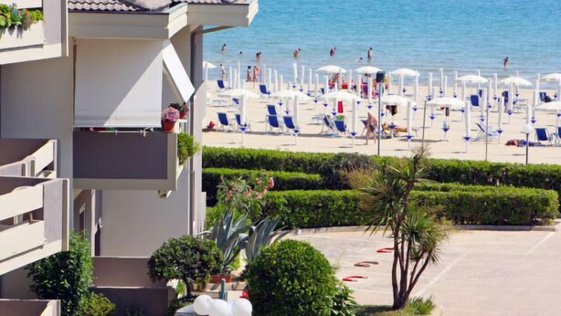 Un hotel con balcón con vistas a una playa que tiene sillas y sombrillas.