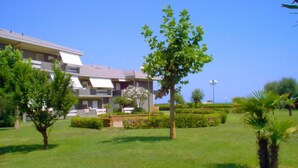 Un edificio residencial con techo plano, varios balcones y un césped cuidado con árboles y arbustos.