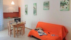 Un espacio de sala pequeño y acogedor, con zona de comedor, un sofá cubierto con una manta naranja y tres obras de arte colgadas en la pared.