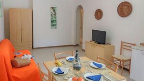 Un comedor con una mesa dispuesta para dos, un televisor en un mueble bajo y un armario al fondo.