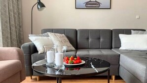 Un salon moderne avec un canapé gris, une table basse noire avec un plateau en verre et un tableau encadré au mur.