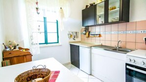 Een keuken met witte kastjes, een fornuis en een gootsteen. Er is een raam met gordijnen en een mandje op het aanrecht.