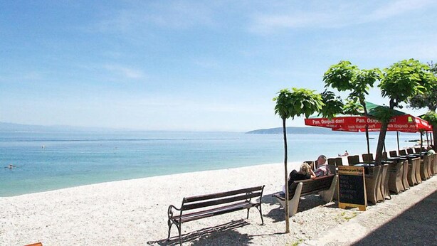 Een strand met een bankje en parasols, een bord en uitzicht op zee.
