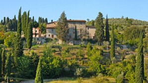 Un bâtiment en pierre, doté d’un toit en tuiles, entouré d’arbres et de végétation sur le flanc d’une colline.