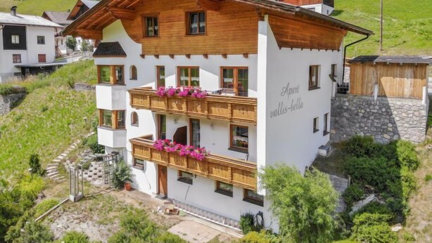 Un immeuble à plusieurs étages doté de balcons en bois, entouré de verdure et d’autres bâtiments.