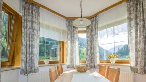 Un coin repas avec une table en bois, des chaises, un luminaire suspendu et de grandes fenêtres avec des rideaux.