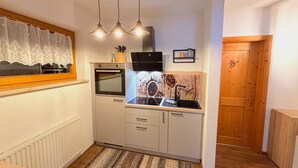 Une cuisine compacte équipée d’un four encastré, d’un micro-ondes, d’un évier et d’une porte en bois portant l’inscription « Chambre ».