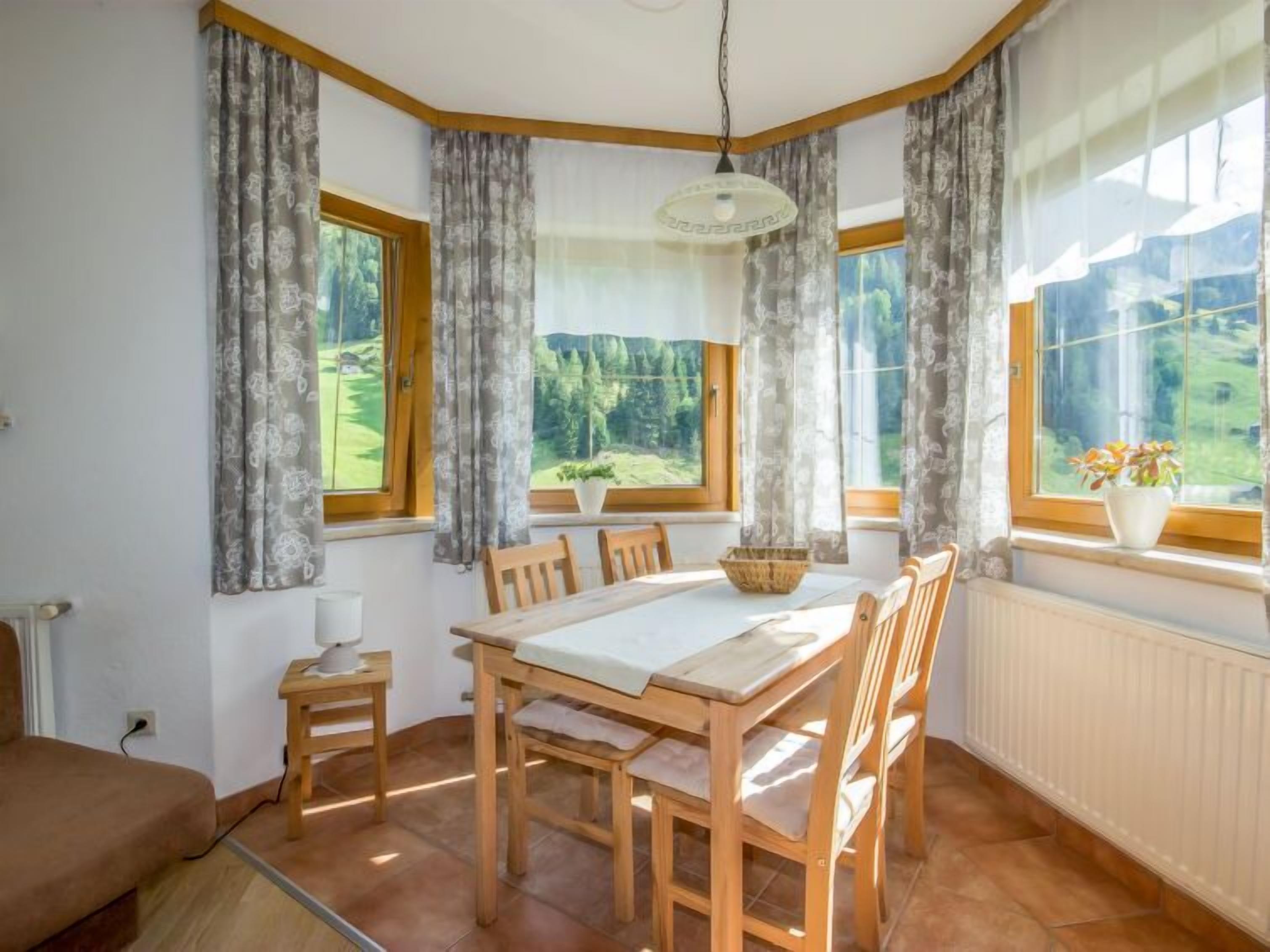 Ruokailutila, jossa on puinen pöytä ja tuolit, suuret ikkunat, joissa on verhot, ja näkymä vehreään maisemaan.