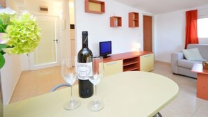 Un saló modern amb una taula de dinar, dues copes de vi i una ampolla de vi. Hi ha un televisor sobre un suport, un sofà i un petit armari.