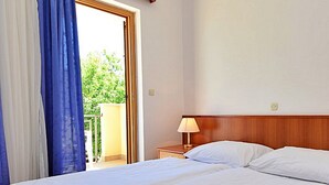 A hotel room with a bed, a nightstand, a lamp, and a view of greenery outside. - Meridiana by Interhome (Orebic)