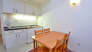 A compact kitchen with white cabinets, a wooden dining table, and a red rug. - Meridiana by Interhome (Orebic)