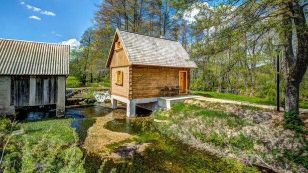 A wooden cabin with a sloped roof, a small porch, and a stream flowing nearby. - Plitvice II by Interhome (Plitvice)