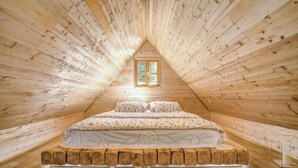 A cozy attic bedroom with a sloped wooden ceiling, a bed with patterned bedding, and a small window. - Plitvice II by Interhome (Plitvice)