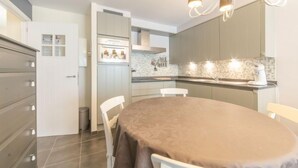 Una cocina moderna con comedor, que cuenta con una isla central, armarios blancos y una araña.