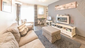 Una sala de estar moderna con un sofá color beige, una alfombra gris, un televisor y una pequeña mesa con una lámpara.