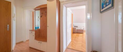 Um corredor com piso de madeira, um guarda-roupa, um espelho e uma porta que dá para um quarto.
