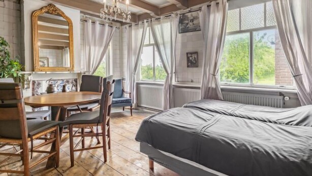 A room with a bed, a table with chairs, a chandelier, and a window with curtains. - Groepswoning De Appelgaard by Interhome (Zaamslag)
