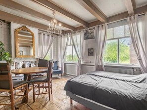 A room with a bed, a table with chairs, a chandelier, and a window with curtains.