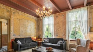 A room with a wooden ceiling, a chandelier, two sofas, a coffee table with fruit, and large windows with curtains. - Groepswoning De Appelgaard by Interhome (Zaamslag)