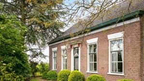 A brick building with a green roof, white window frames, and a well-maintained lawn with trimmed bushes. - Groepswoning De Appelgaard by Interhome (Zaamslag)