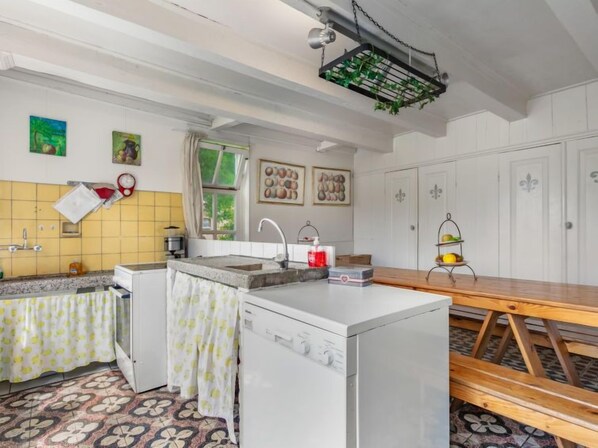 A compact kitchen with a central island, a sink, and a stove. There is a wooden table and benches in the dining area.