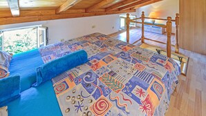 A room with a wooden ceiling, a colorful patterned bedspread, a blue sofa, and a wooden chair. - Karolina by Interhome (Lovran)