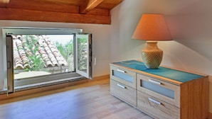 A room with a wooden ceiling, a sliding glass door leading to a balcony, a wooden cabinet with drawers, and a table lamp. - Karolina by Interhome (Lovran)