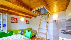 A room with a wooden ceiling, a green sofa, a dining table with chairs, a wooden ladder, and a kitchen area with a sink. - Karolina by Interhome (Lovran)
