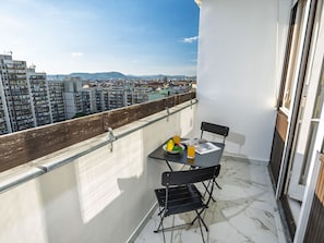 Enjoy a city view from this balcony with a table, chairs, and a refreshing breakfast setup.
