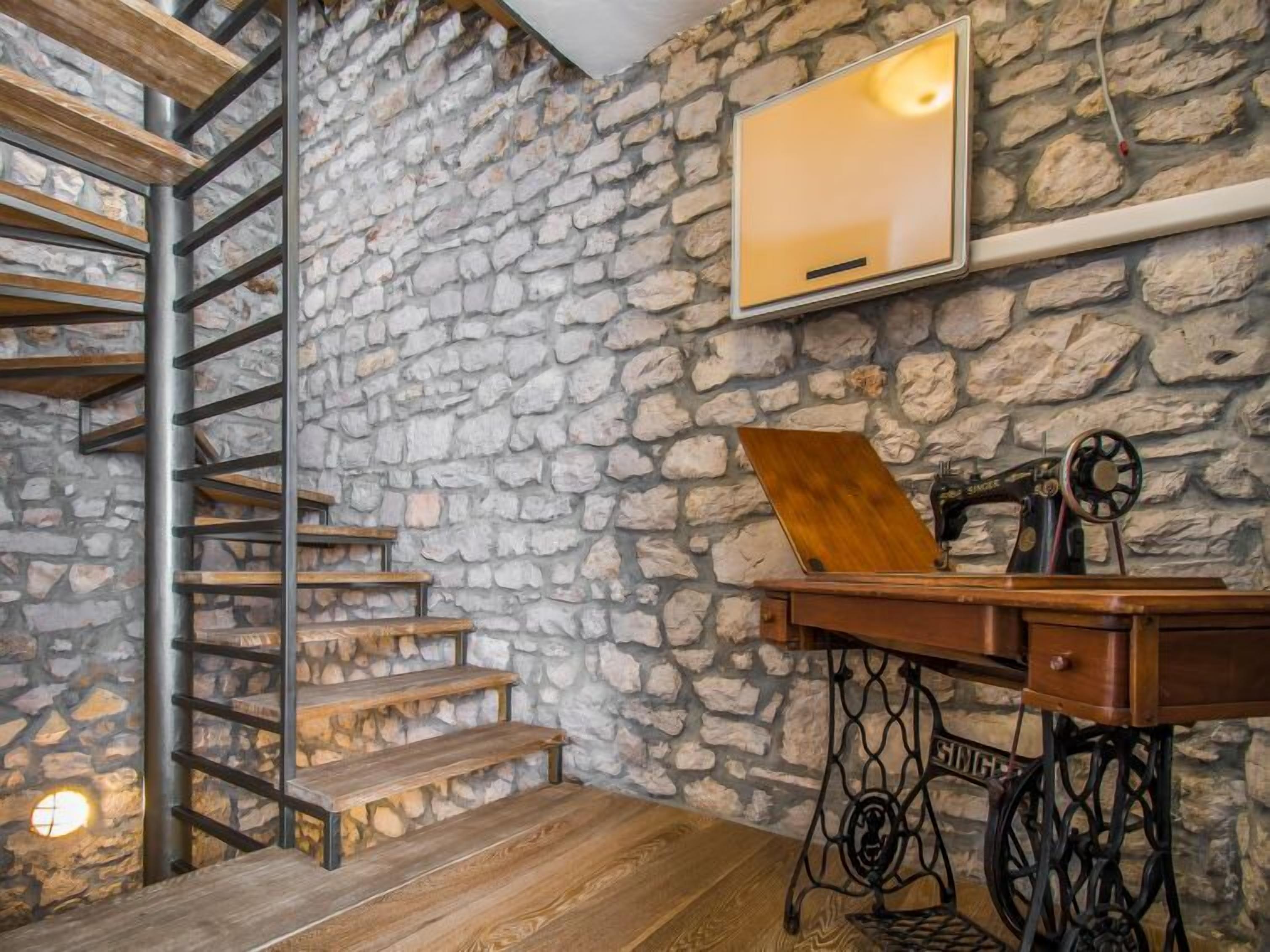 A rustic room with a stone wall, wooden staircase, and a sewing machine.