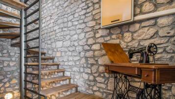 A rustic room with a stone wall, wooden staircase, and a sewing machine.