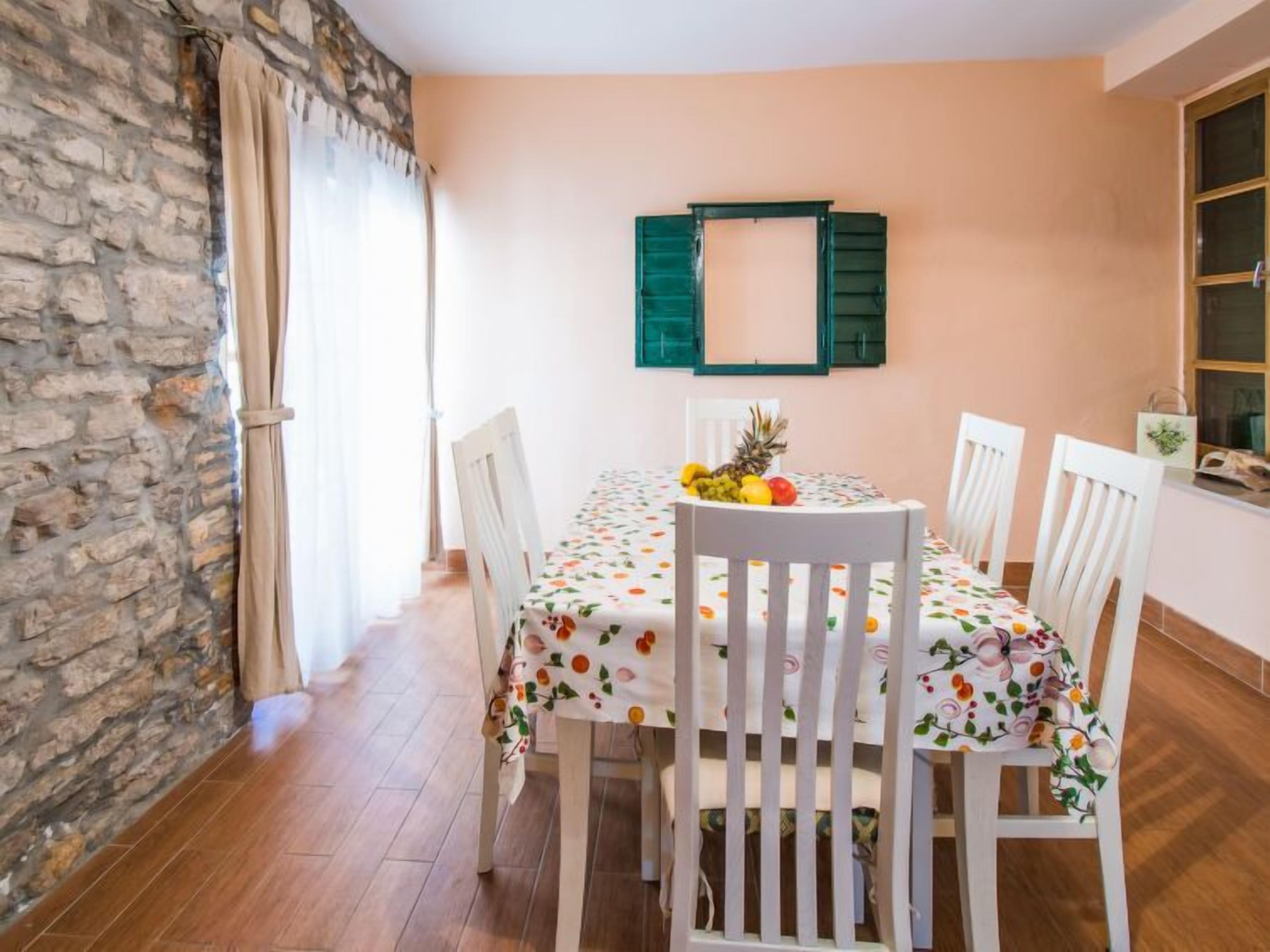 Een eetruimte met een ronde tafel, witte stoelen en een tafelkleed met bloemen.