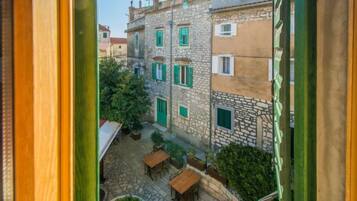 A courtyard with stone flooring, wooden tables, and green shutters on buildings.