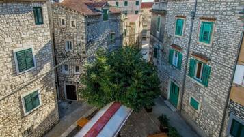 A narrow street with stone buildings, green shutters, and outdoor seating.