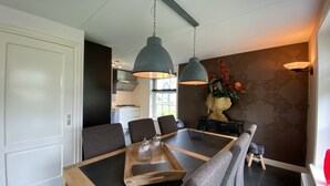 Zona pranzo con tavolo in legno, sedie rivestite di grigio e illuminazione a sospensione.