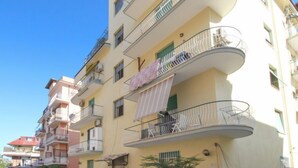 Un immeuble résidentiel à plusieurs étages, doté de balcons, avec un espace de stationnement à l’avant et un ciel dégagé.