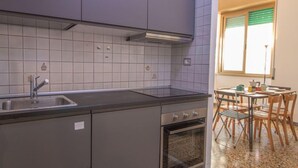 Une cuisine compacte équipée d’un évier, d’une cuisinière et d’un four, jouxtant un coin repas avec une table et des chaises.