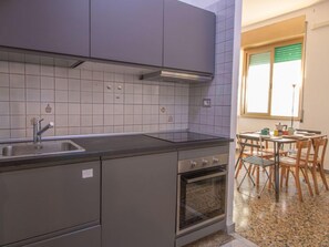 A compact kitchen with a sink, stove, and oven, adjacent to a dining area with a table and chairs. - Aurelia by Interhome (Rome)