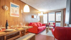 A cozy room with wooden walls, a wooden dining table set for two, a red sofa, and a red armchair.
