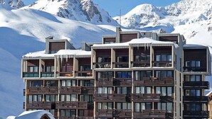 A modern multi-story hotel with balconies, set against a snowy mountain backdrop.
