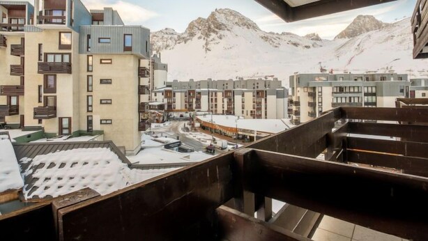A snow-covered mountain town with modern buildings, including a multi-story hotel with balconies and a view of the mountains.