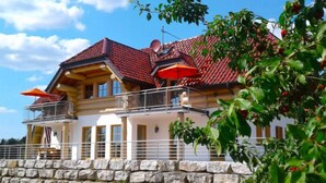 A two-story building with a stone wall foundation, a red-tiled roof, and a balcony with a railing.