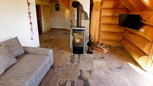 A cozy log cabin interior with a stone fireplace, wooden walls, a grey sofa, and a television mounted on the wall.