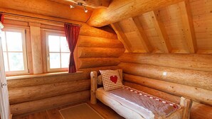 A log cabin room with a loft bed, wooden walls, and a window with curtains.