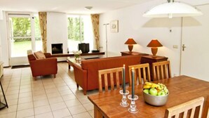 A spacious living area with a sofa, a dining table with chairs, a TV, and a fireplace. - Vacation home 2+ by Interhome (Lochem)