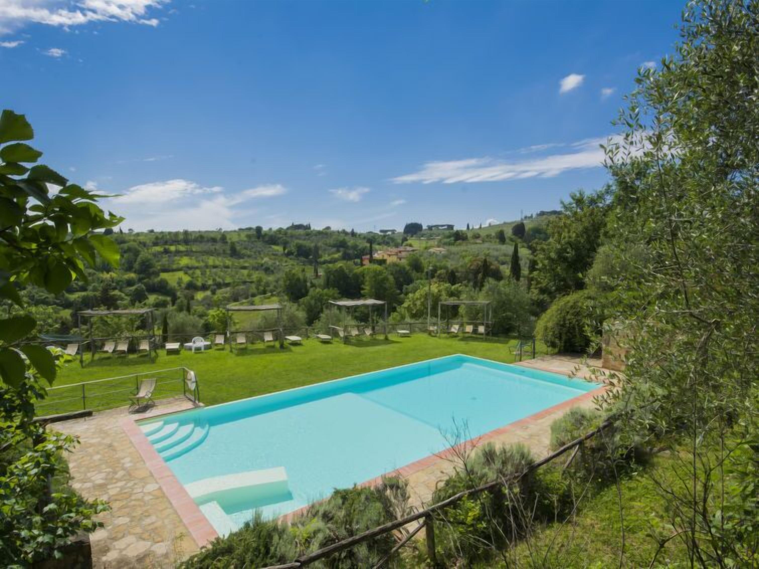 Ein rechteckiger Pool mit Steinumrandung, umgeben von einer Rasenfläche mit Liegestühlen und einer Pergola.